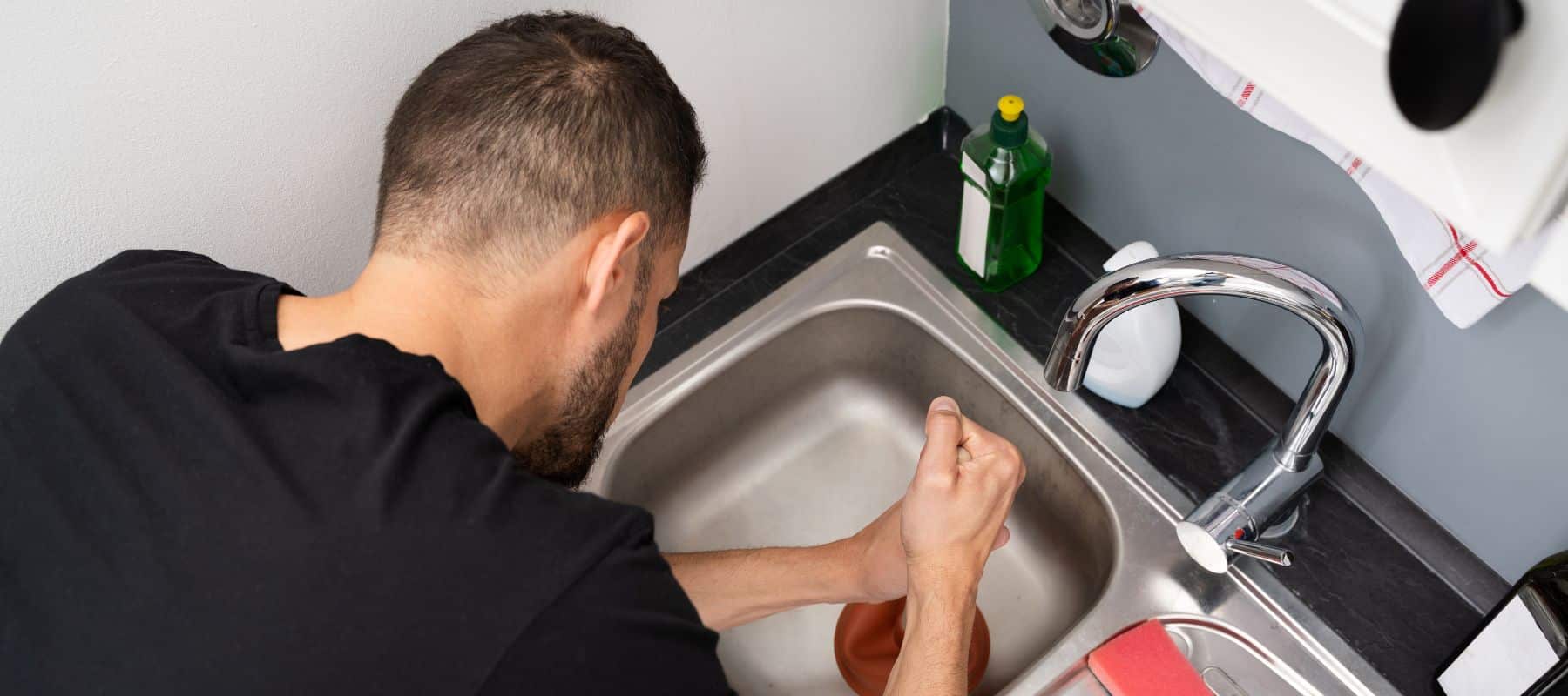 a man using a plumber on a kitchen sink to clear a clogged drain